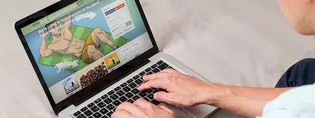 A person's hands typing on a laptop with the wikiHow home page on the screen.